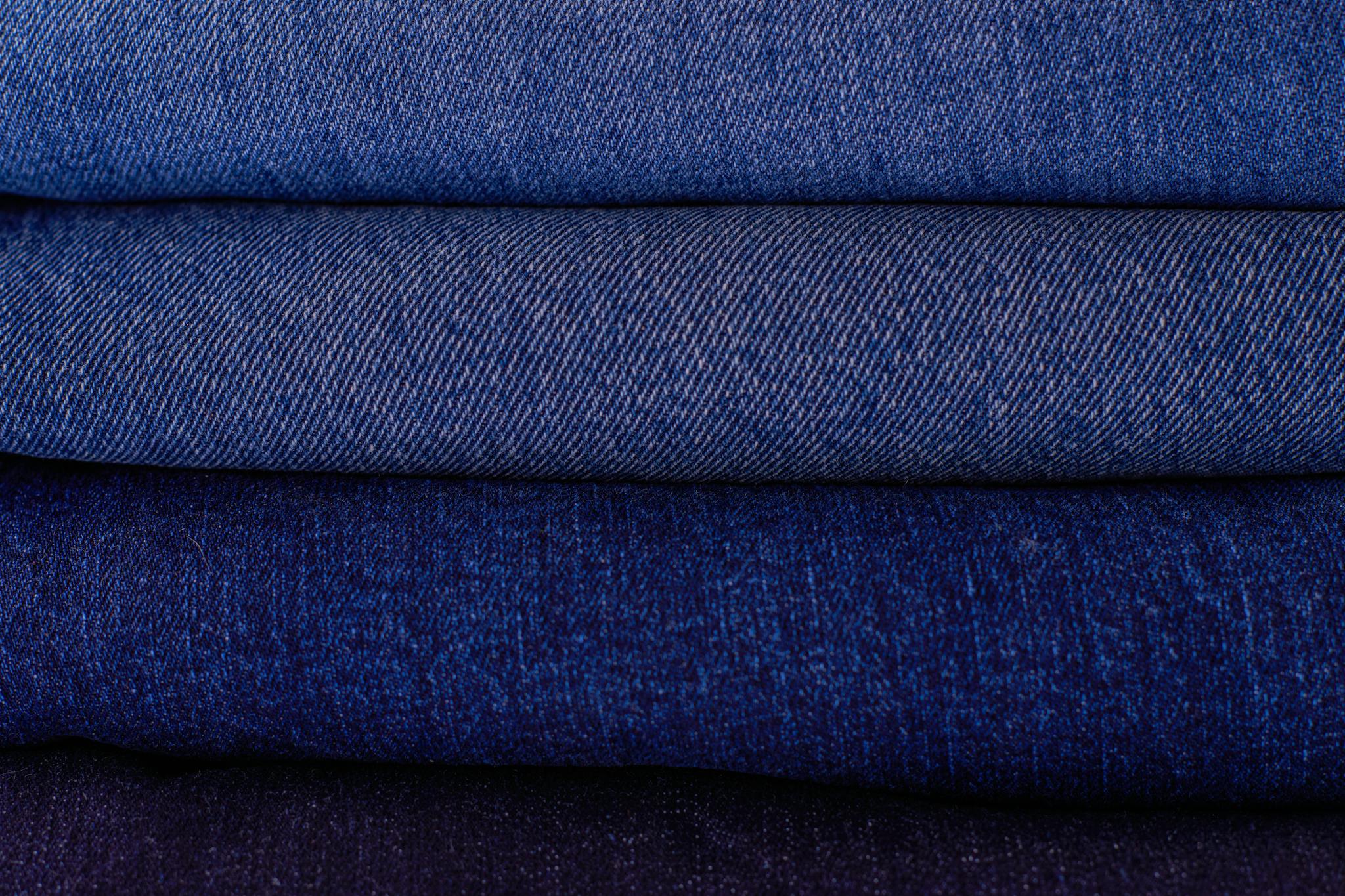 Close-up of neatly stacked folded denim fabrics in varying blue tones showcasing texture and pattern.