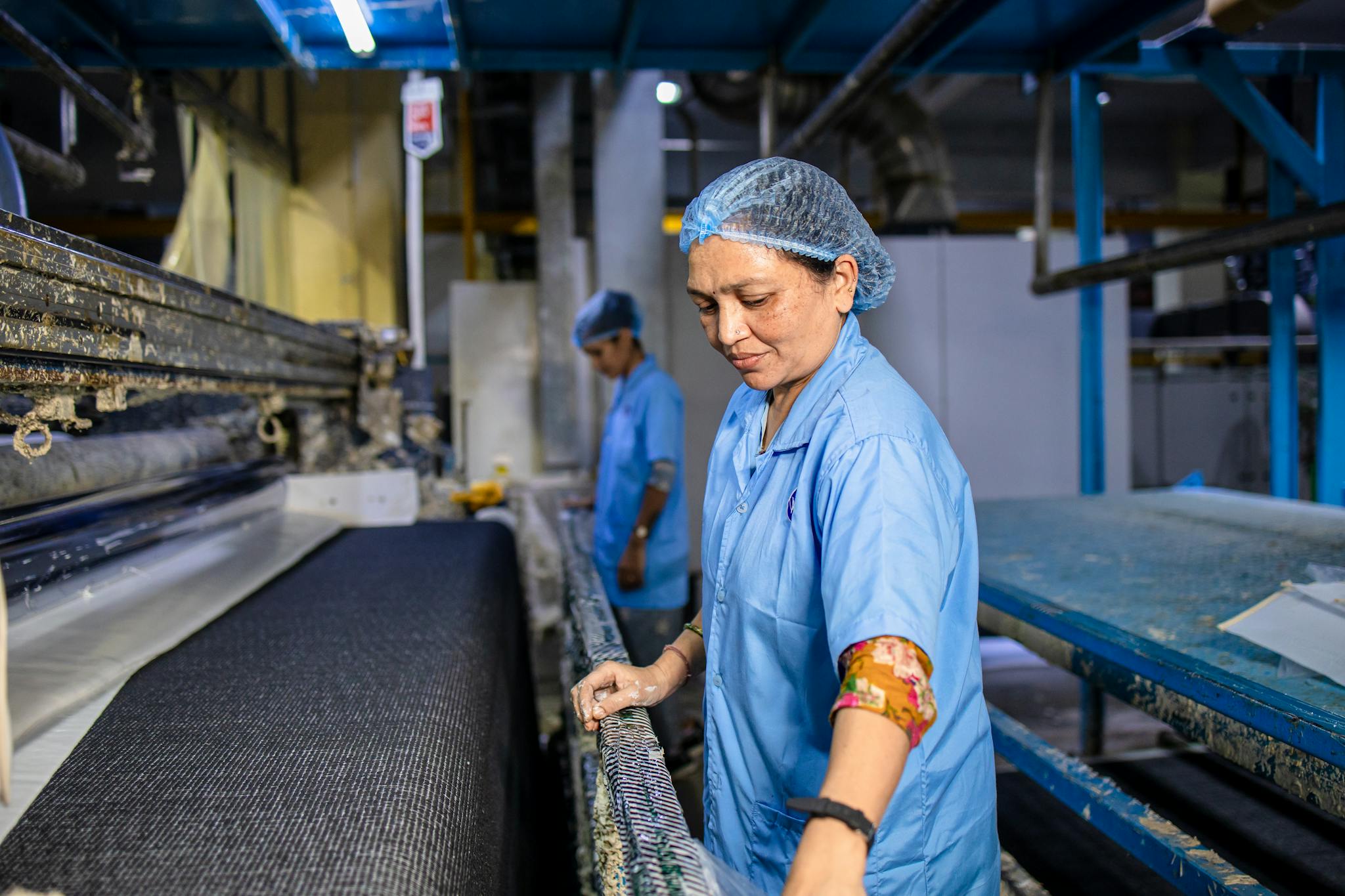 Textile workers operate machinery in a modern factory setting, focusing on quality control and production efficiency.
