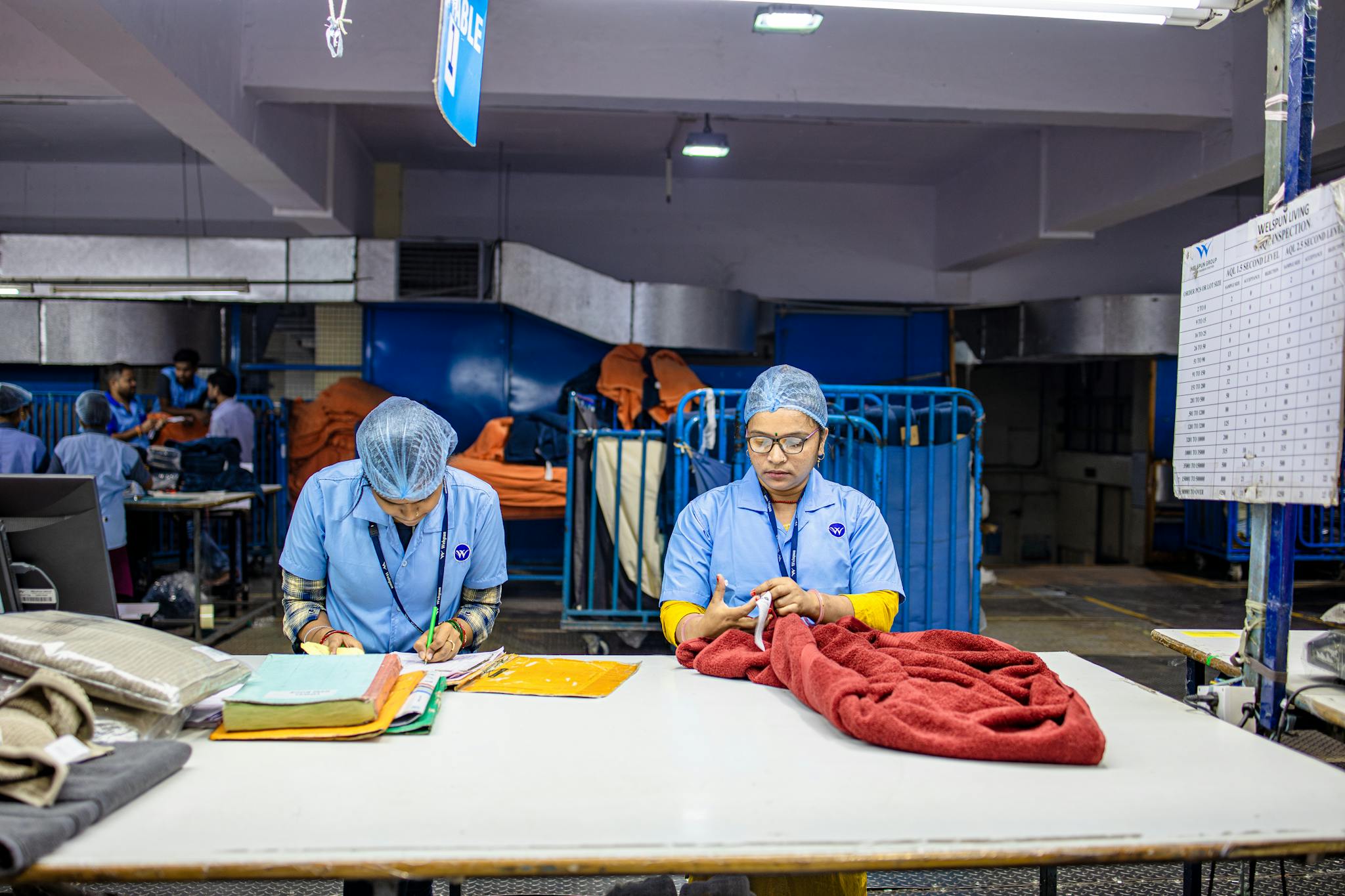 Two workers in a textile factory sorting fabric at a table under bright lighting.